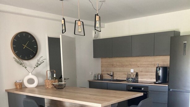 Une cuisine moderne dotée d’un îlot central, de tabourets de bar, d’une horloge et d’une machine à café.