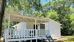 A white cabin with a porch and a covered area, surrounded by trees. - Country and quiet place, for get a great vacation (Splendora)