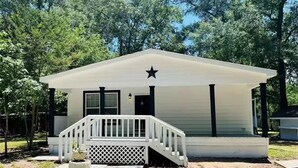 A small, single-story house with a white exterior, a front porch with a white railing, and a black star on the roof. - Country and quiet place, for get a great vacation (Splendora)