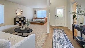 A spacious living room with a sofa, coffee table, and a bookshelf. There is a bedroom with a bed and a window. A door leads to another room. - Spotless Modern Spacious 1 min to Hurricane Ridge entrance Patio Family friendly (Port Angeles)