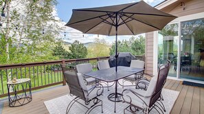 A covered outdoor patio with a table and chairs, a grill, and a view of the surrounding landscape.