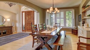 A dining area with a wooden table, chairs, a chandelier, and a view of the outdoors.