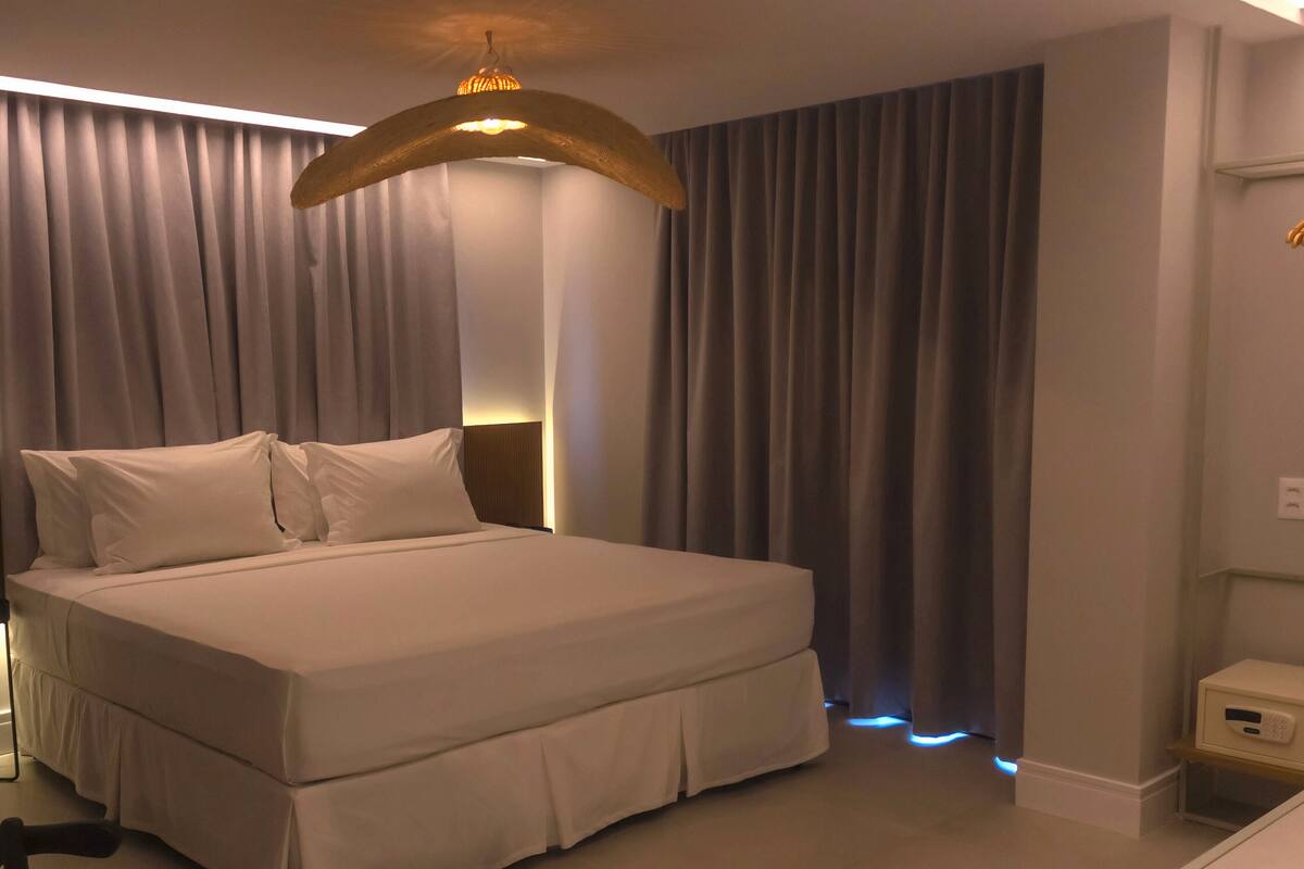 A neatly made bed with white linens, a wooden headboard, and a modern pendant light.