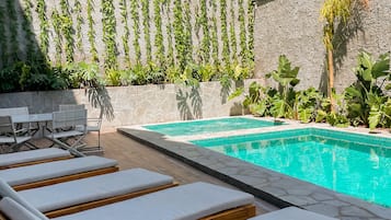 A poolside area with lounge chairs and a stone wall with climbing plants.