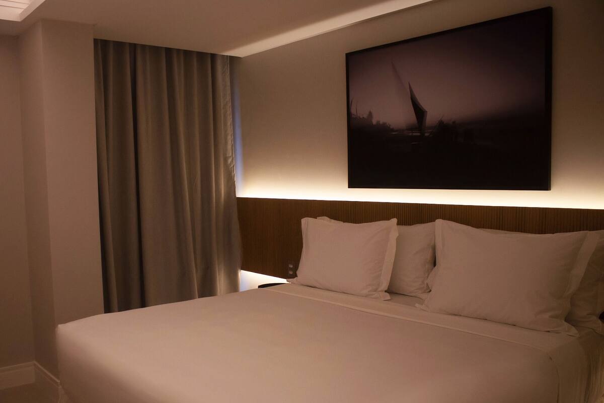 A hotel room with a large bed, a headboard, and a painting on the wall.