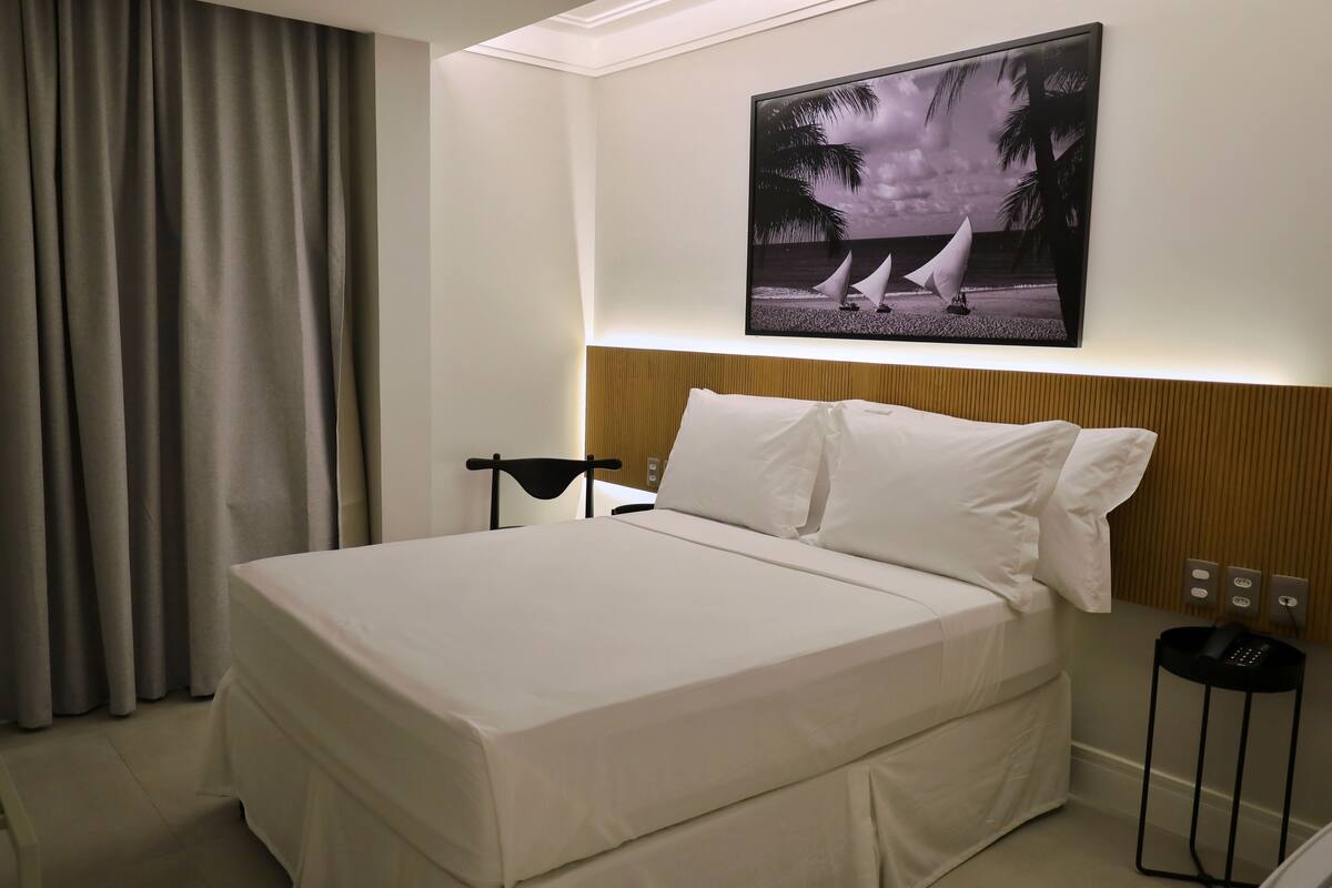 A hotel room with a bed, a nightstand, a wall-mounted TV, and a curtain.