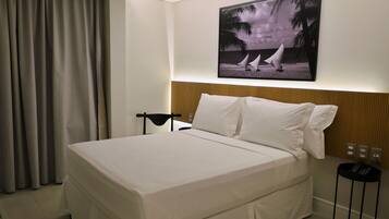 Una habitación de hotel con cama, mesita de noche, televisor montado en la pared y cortina.