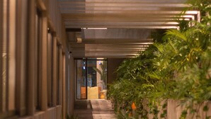 Un pasillo con techo de hormigón, una puerta de cristal al final y plantas verdes a lo largo de las paredes.