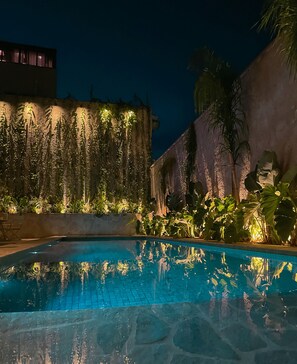 A nighttime pool area with a clear pool, surrounding plants, and a building with illuminated walls. - Tintto Hotel (Fortaleza)