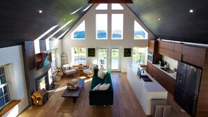 A spacious living area with a fireplace, a green sofa, and a kitchen with modern appliances. - Au Bon Orchard - Catskills Mountain Views/Private Heated Pool and Jacuzzi (Parksville)