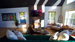 A modern living room with a fireplace, green sofa, and a painting on the wall. - Au Bon Orchard - Catskills Mountain Views/Private Heated Pool and Jacuzzi (Parksville)