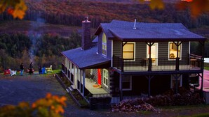A two-story cabin with a porch and a deck, surrounded by a forested landscape. - Au Bon Orchard - Catskills Mountain Views/Private Heated Pool and Jacuzzi (Parksville)