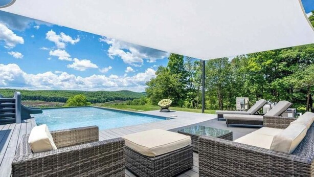 A poolside area with wicker furniture, a glass table, and a view of a lake and hills. - Au Bon Orchard - Catskills Mountain Views/Private Heated Pool and Jacuzzi (Parksville)