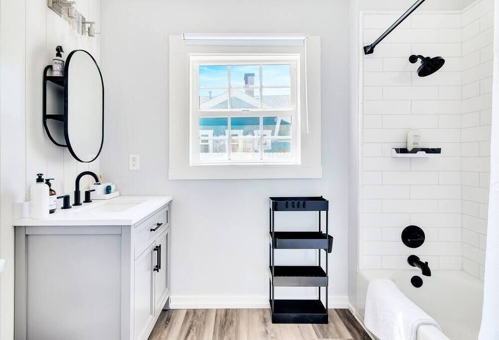 Une salle de bain moderne avec un meuble-lavabo blanc, une étagère noire, une fenêtre donnant sur un beau paysage et un espace douche.