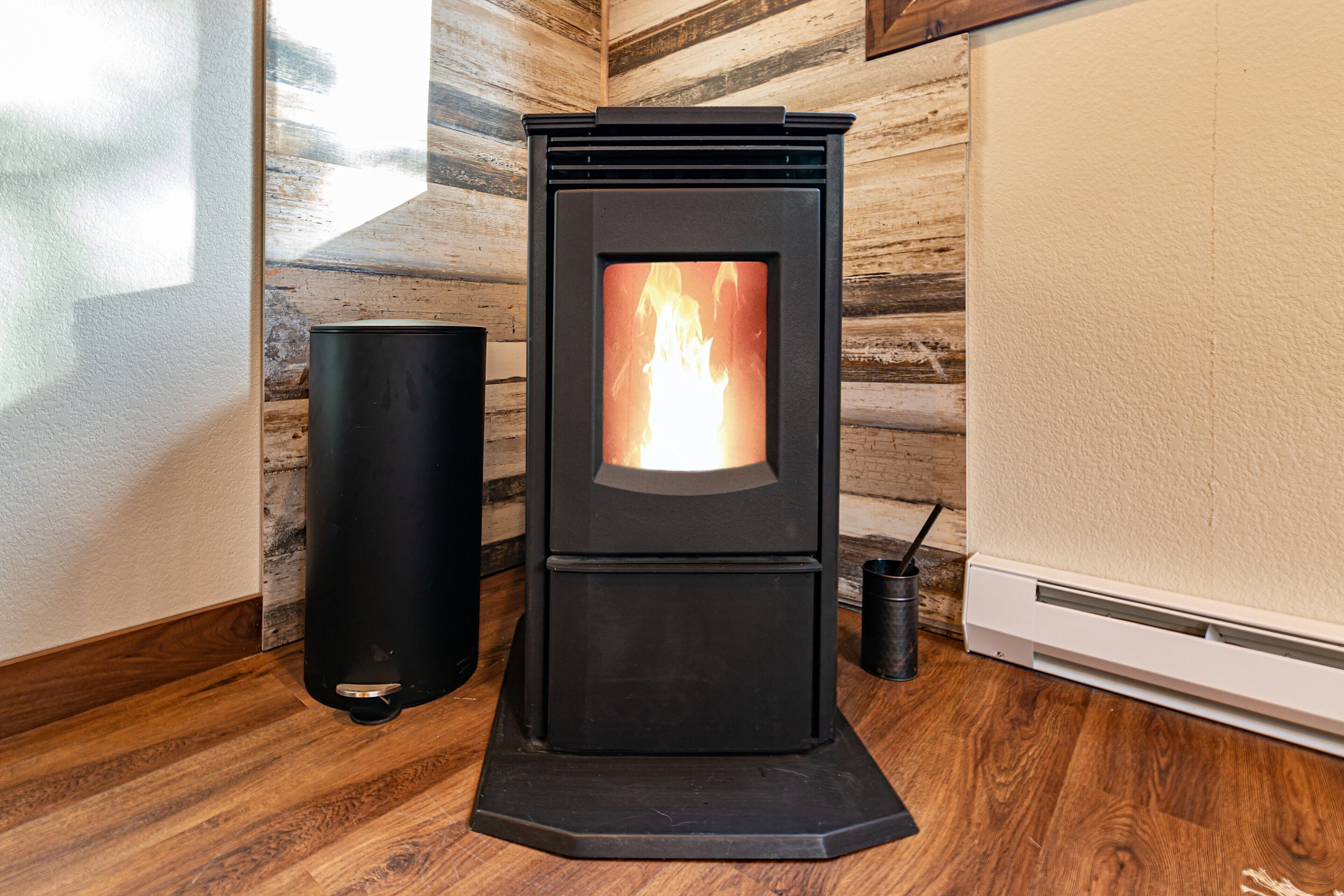 A wood-burning stove with a visible fire, a black cylindrical object beside it, and a wooden wall in the background.