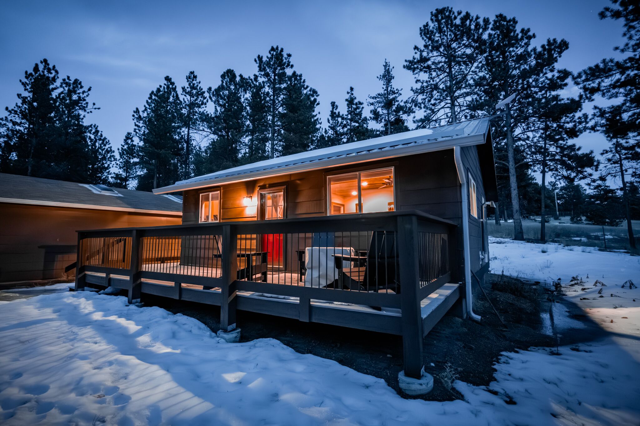 A two-story cabin with a deck, surrounded by snow and trees.
