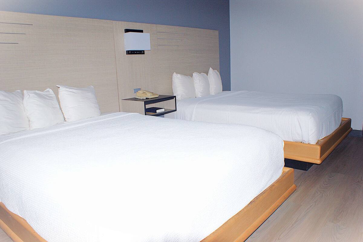 Hotellihuone, jossa on kaksi sänkyä, yöpöytä ja seinään kiinnitetty valaisin.