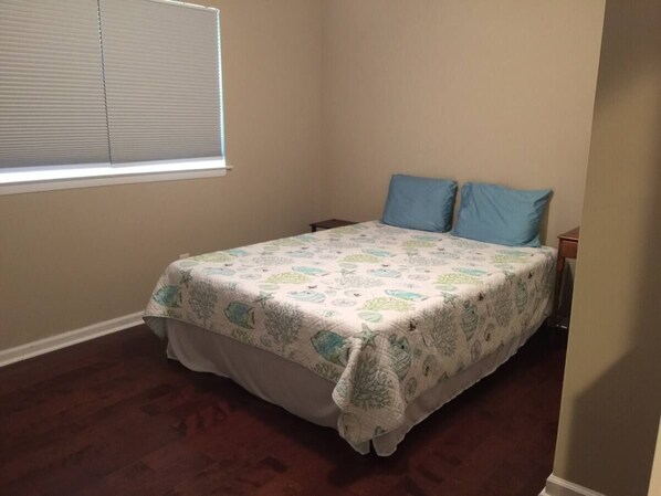 A bedroom with a bed, two pillows, a nightstand, and a window with blinds. - Thunderbolt Home | Clean & Comfortable | Close to Beach and Downtown (Savannah)