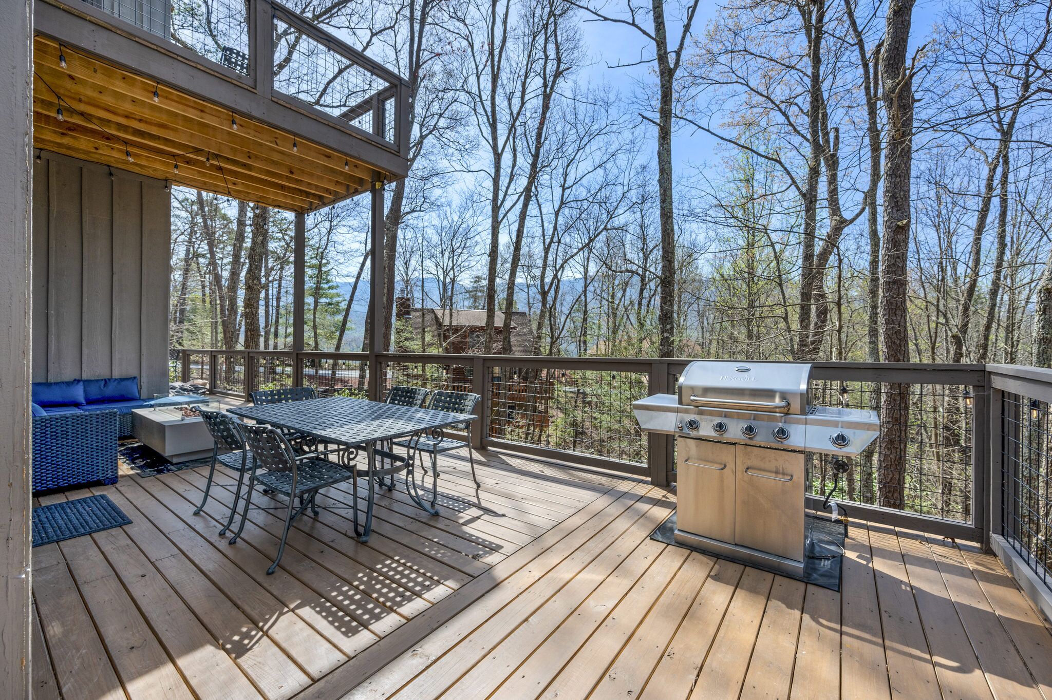 A wooden deck with a grill and outdoor seating area, surrounded by trees.