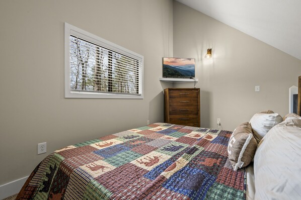 Un dormitorio con una cama grande, una ventana con persianas, un televisor sobre una estantería y un aparador de madera.