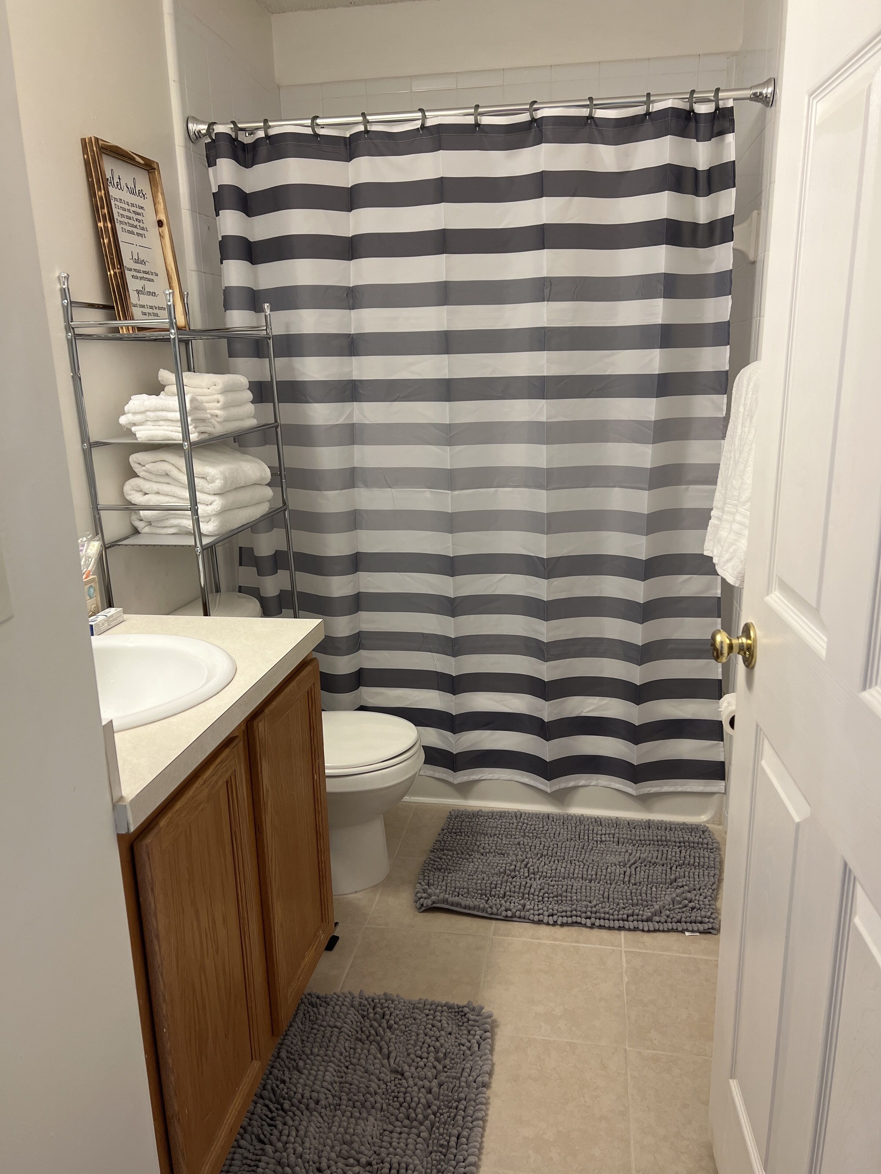Une salle de bain avec un rideau de douche à rayures, des toilettes, un lavabo et un porte-serviettes avec des serviettes pliées.