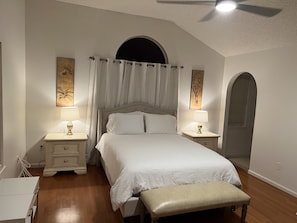 Un dormitorio con una cama grande, dos mesitas de noche con lámparas, un banco y obras de arte en las paredes.