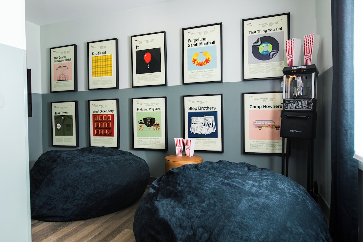 A room with a wall decorated with framed posters, two bean bags, a popcorn machine, and a small wooden table.