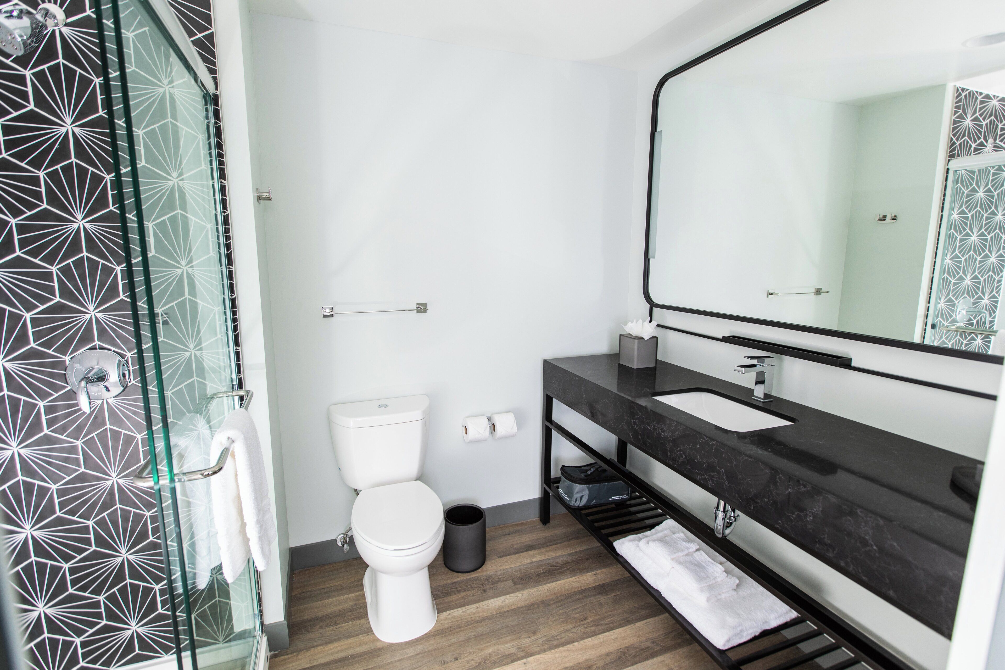 Ein modernes Badezimmer mit Duschkabine aus Glas, einer weißen Toilette, einem schwarzen Marmorwaschbecken und einem großen Spiegel.