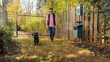 Un home passeja un gos per un pati tancat amb una valla de fusta i un cubell de color verd.