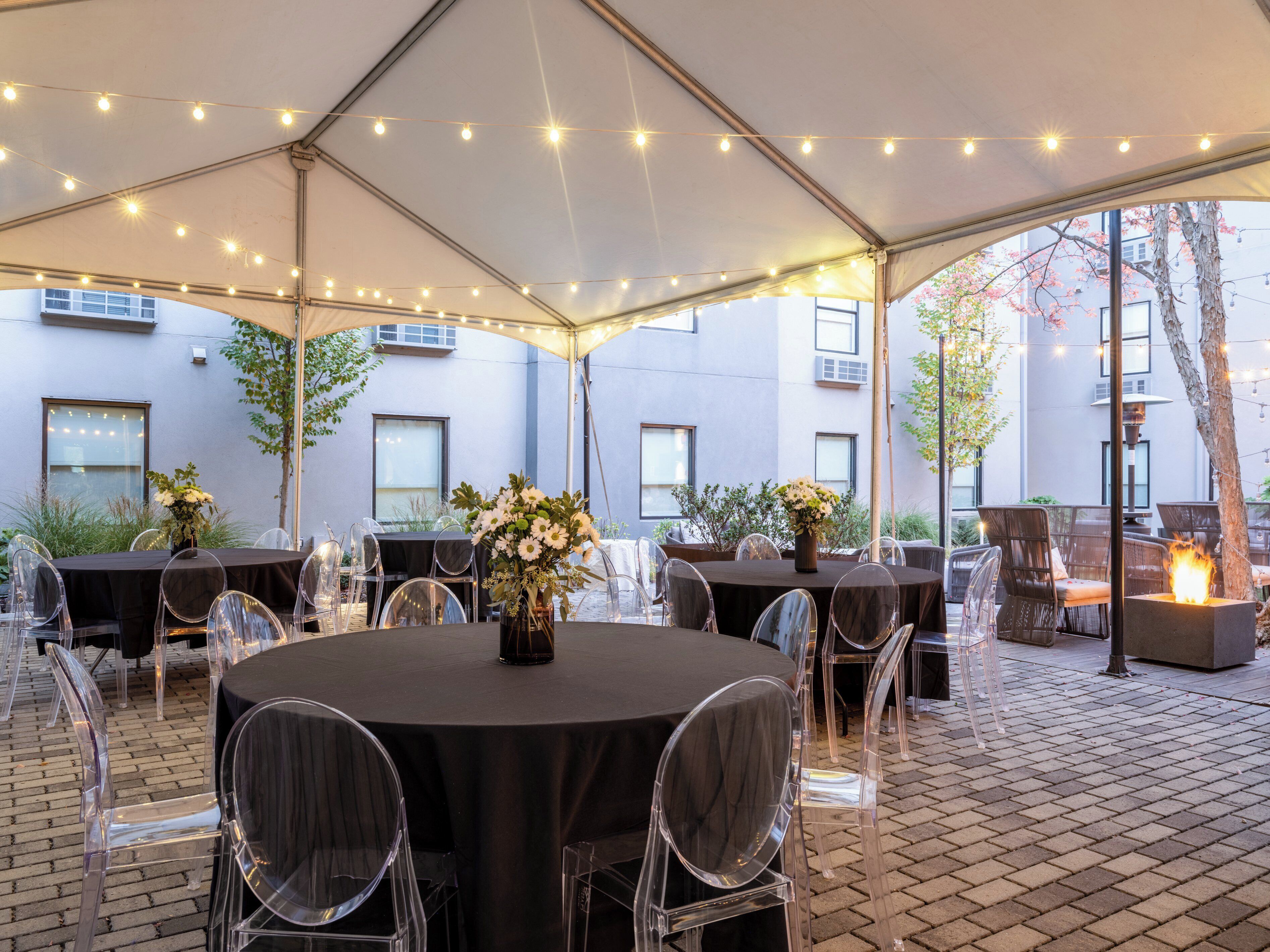 Une terrasse extérieure avec des tables et des chaises rondes, des guirlandes lumineuses et un foyer.