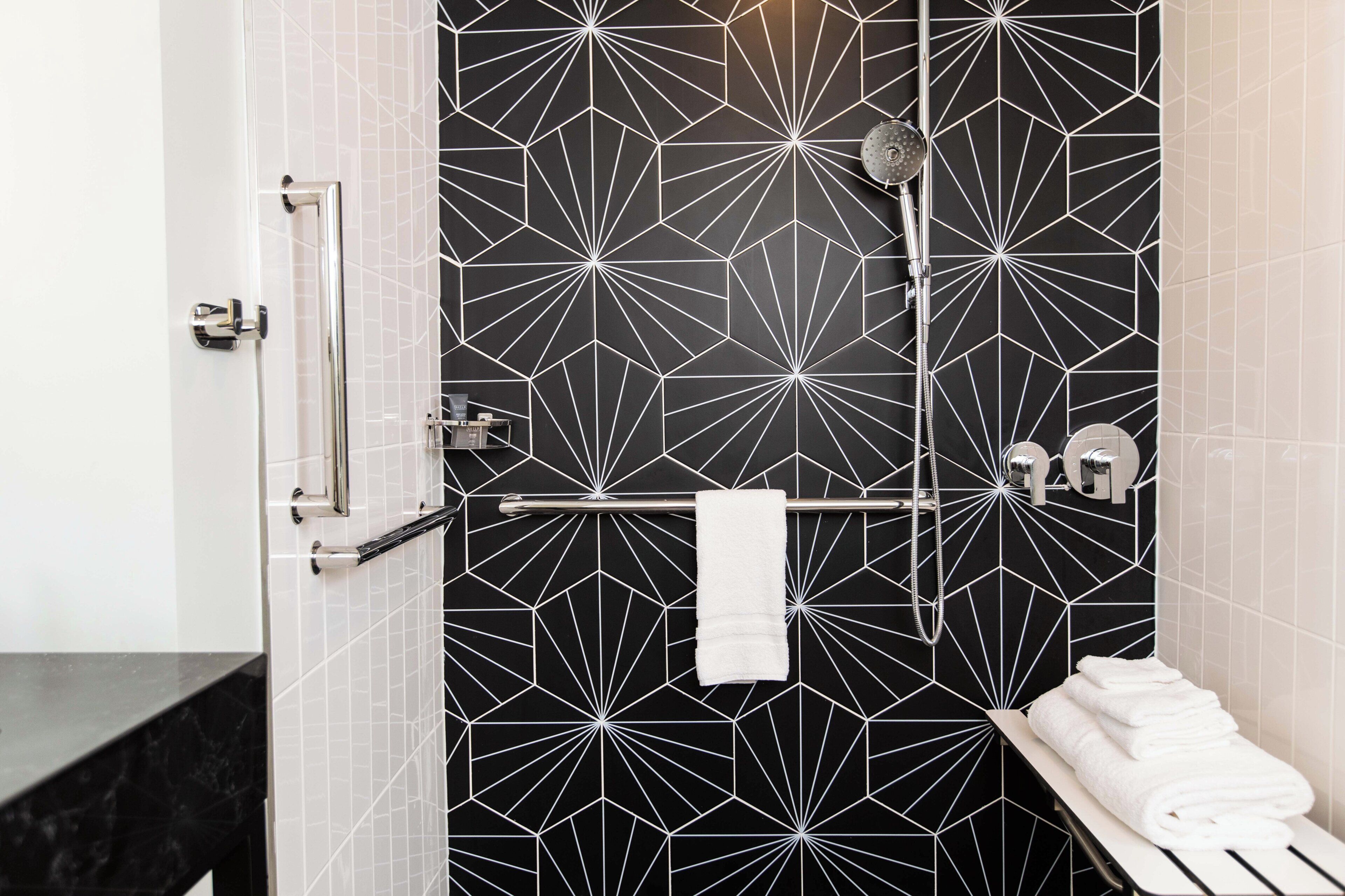 A modern bathroom with a geometric black and white tile backsplash, a glass shower enclosure, and a white towel rack with towels.