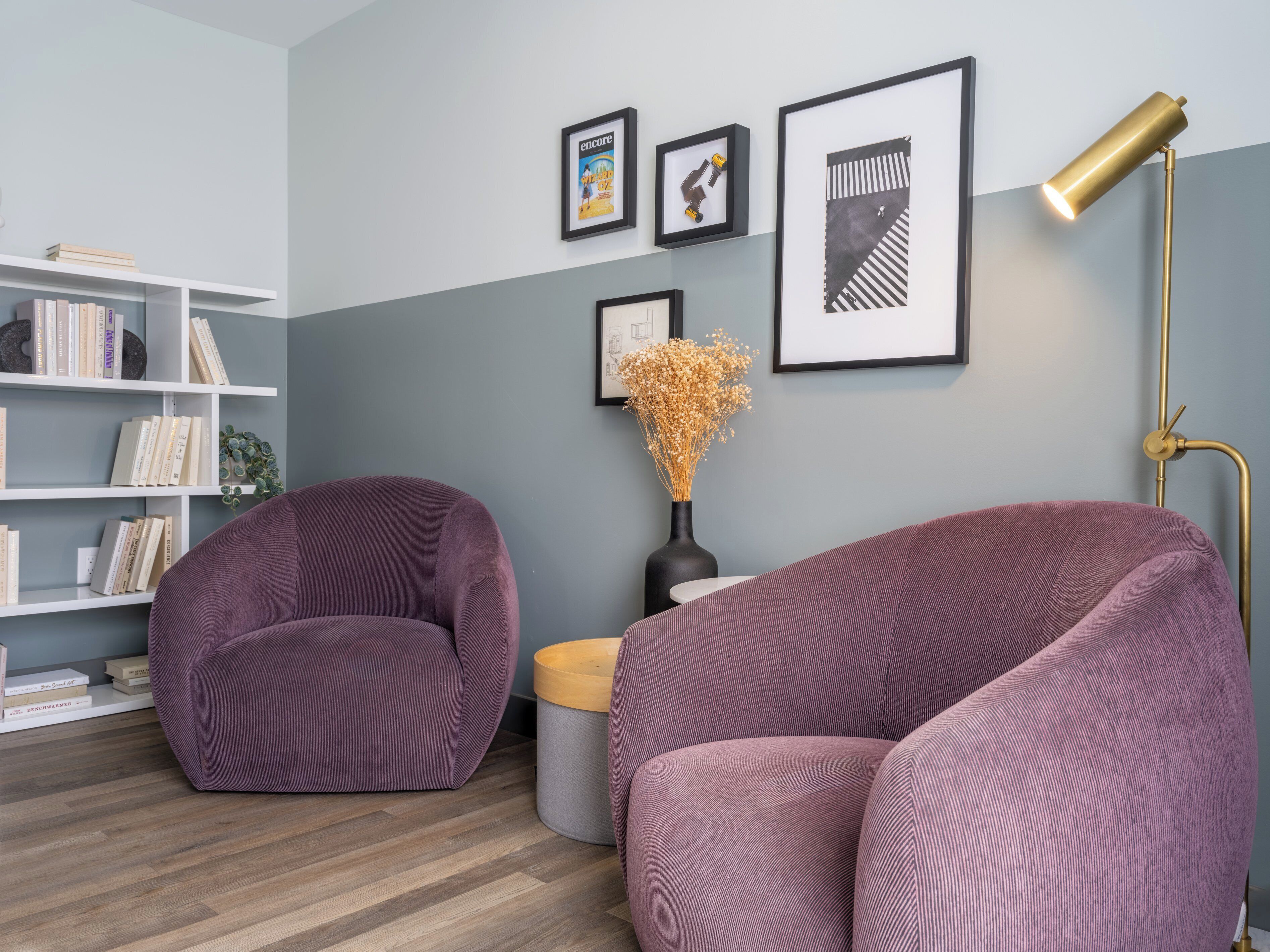 A modern living room with two purple armchairs, a white bookshelf, and a floor lamp.