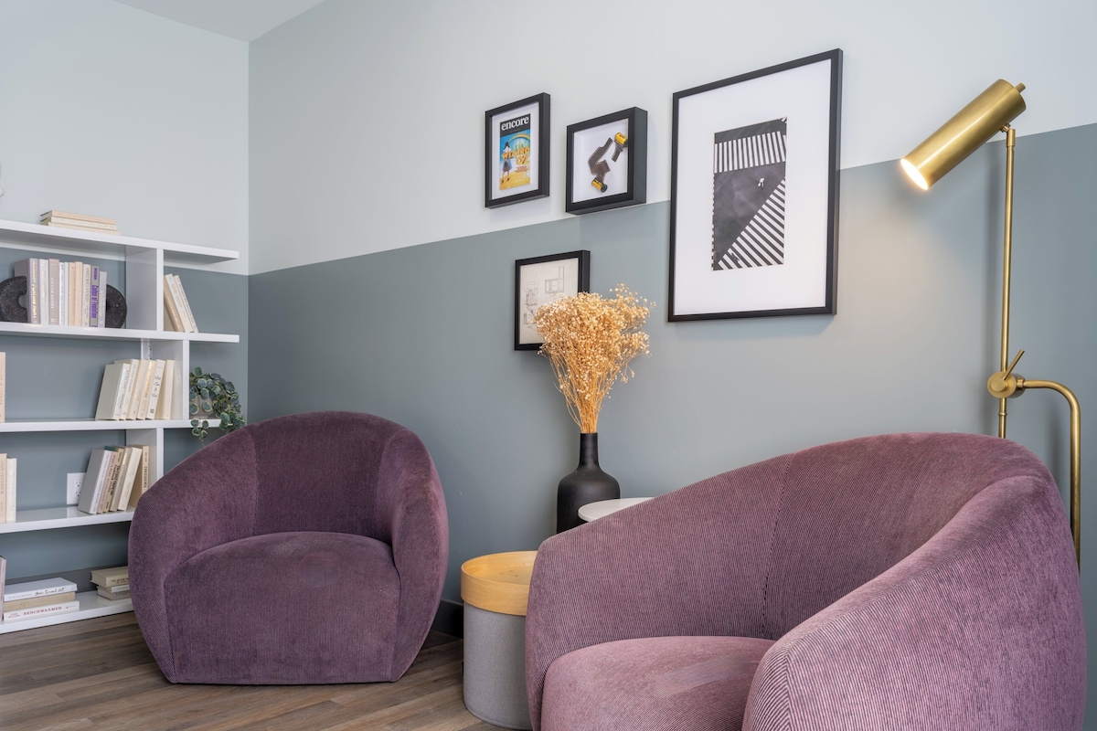 Una sala de estar moderna con dos sillones morados, una estantería blanca y una lámpara de pie.