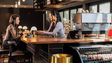 A bar area with a coffee machine, seating, and a trash bin.