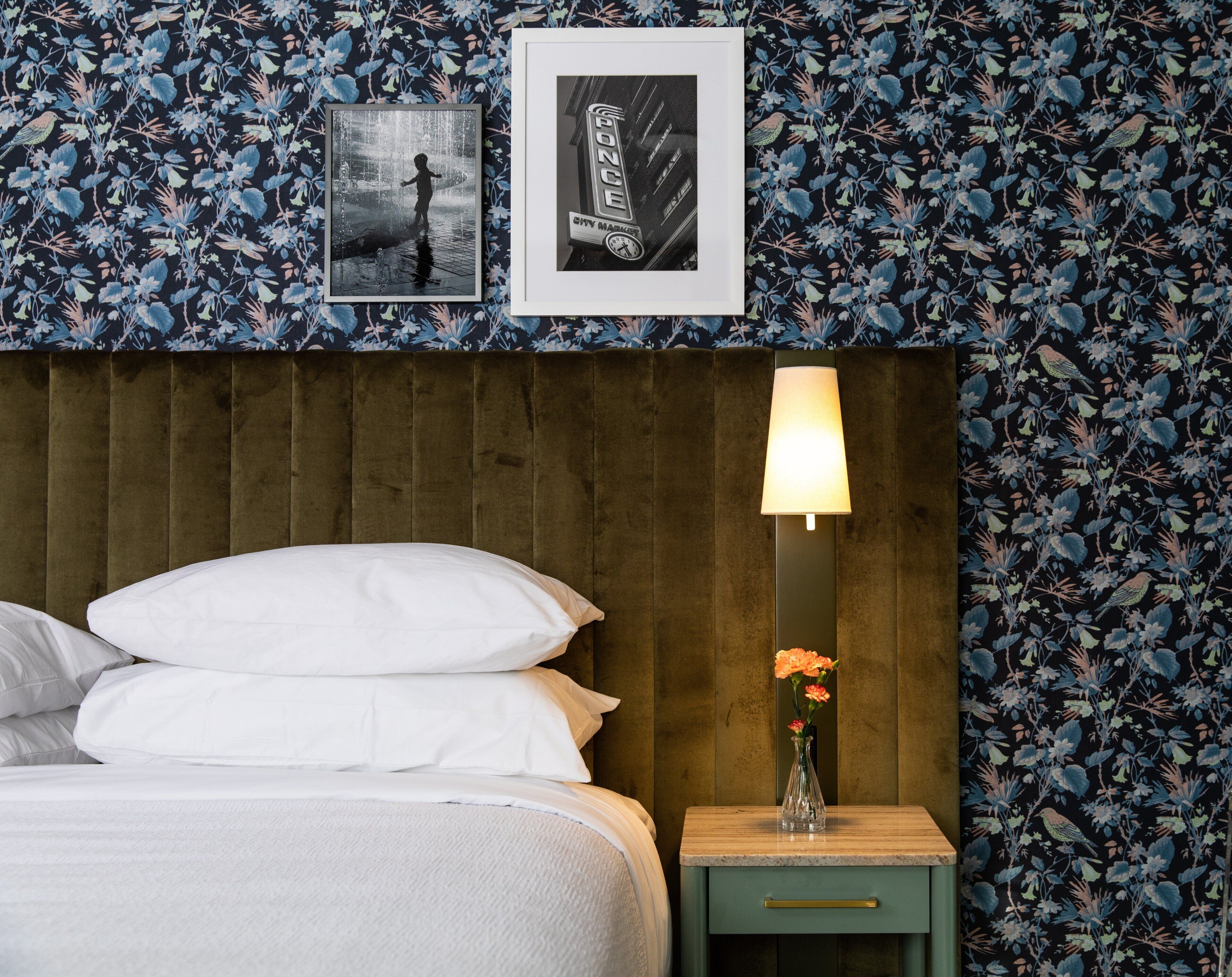 A neatly made bed with white linens, a wooden headboard, a nightstand with a lamp, and a framed picture on the wall.