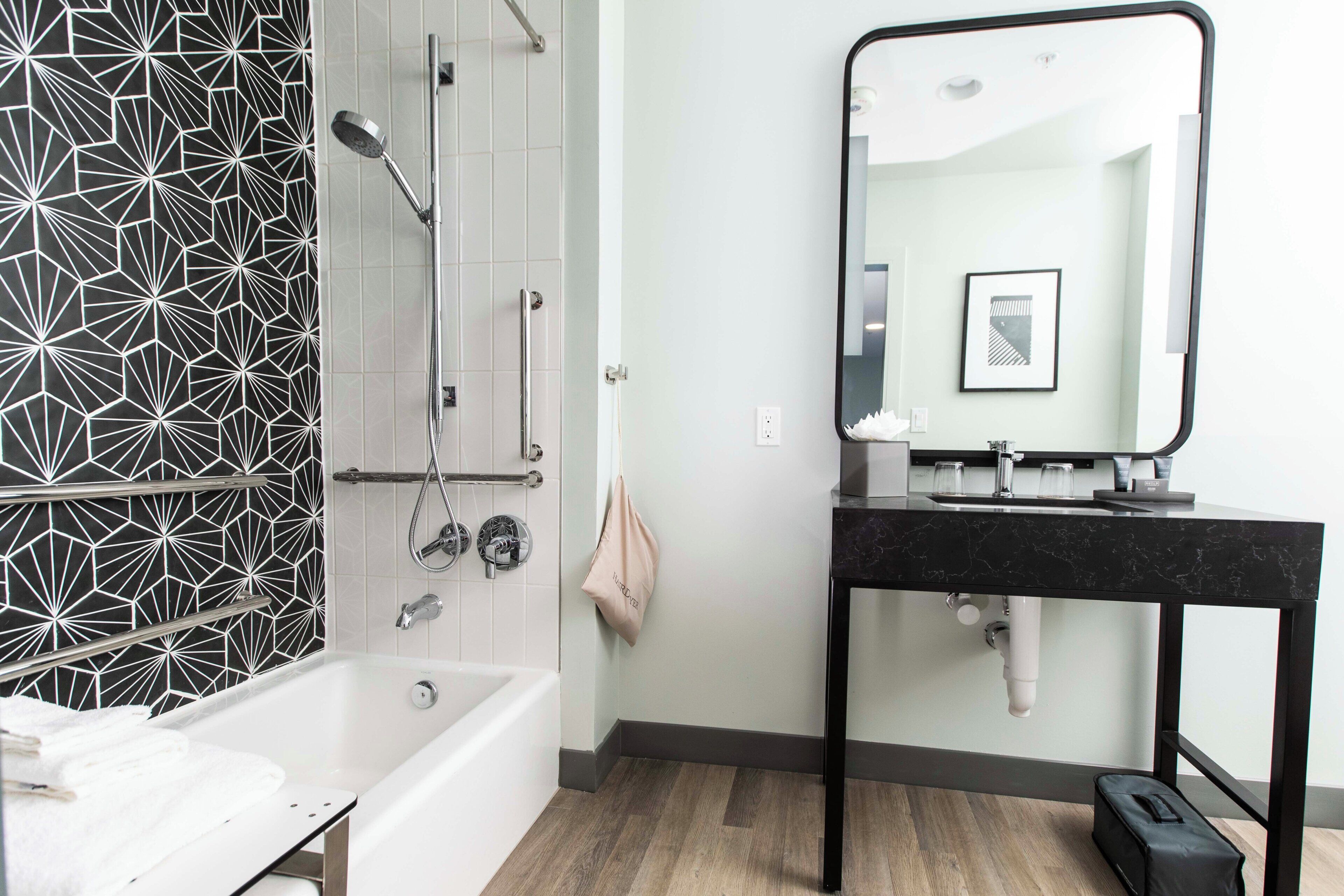 A modern bathroom with a geometric-patterned wall, a freestanding bathtub, a black marble sink, and a mirror above the sink.