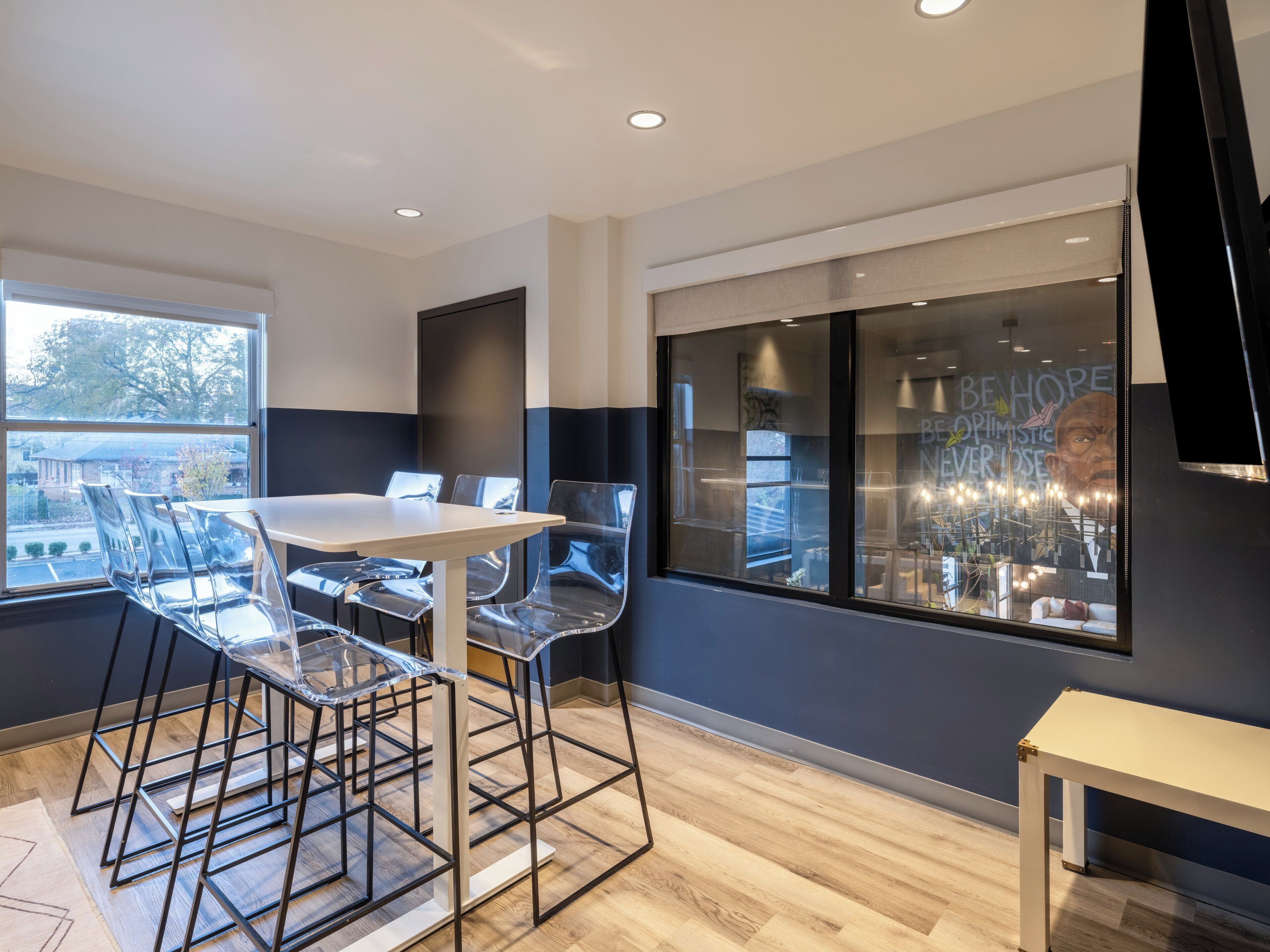 A modern dining area with a table and chairs, a large window with a view, and a television mounted on the wall.