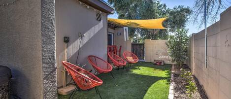 Un jardin avec une pelouse artificielle, des chaises rouges, un parasol jaune et un mur en briques.