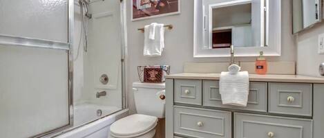 Un baño con ducha, inodoro, tocador y espejo.