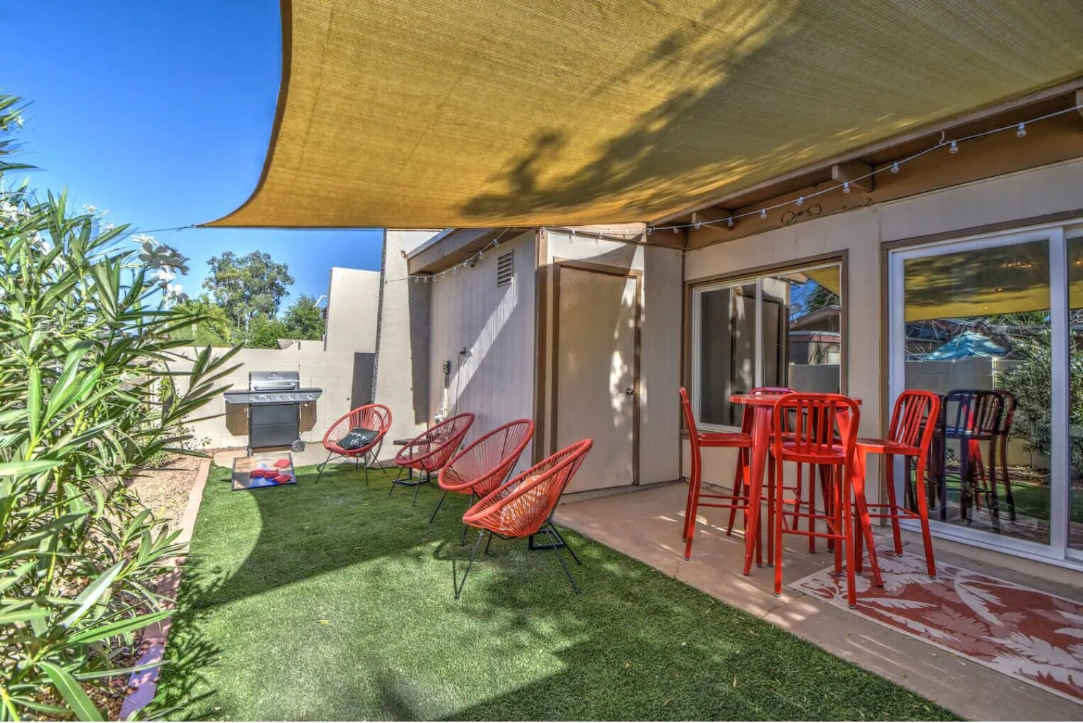 A patio with a barbecue, red chairs, and a table under a shade sail.
