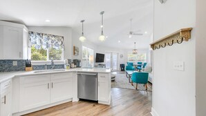 A modern kitchen with white cabinetry, a dishwasher, and a dining area with teal chairs. - ☀️350yd2Beach-Patio-Bikes-Firepit-30A-Dunestruck☀️ (Santa Rosa Beach)