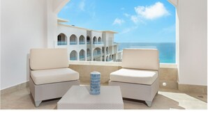 Un balcon avec deux fauteuils confortables et une table, donnant sur un immeuble doté de nombreux balcons et offrant une vue sur la mer.