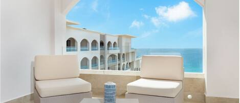 Un balcon avec deux fauteuils confortables et une table, donnant sur un immeuble doté de nombreux balcons et offrant une vue sur la mer.