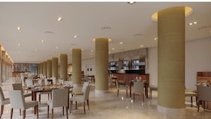 Un vaste espace dédié à la salle à manger, avec de hauts plafonds, plusieurs tables et une cuisine moderne en arrière-plan.