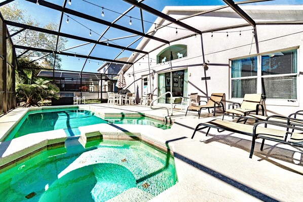 A swimming pool with a glass enclosure, surrounded by lounge chairs and a covered patio area.