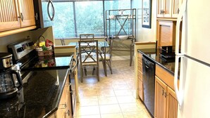 Una cocina con armarios de madera, encimera negra y comedor con mesa y sillas.