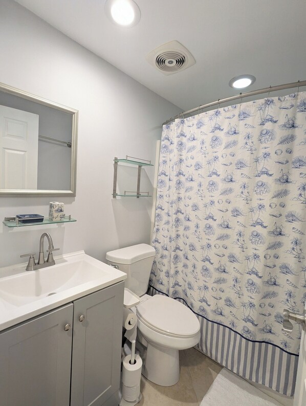 A bathroom with a white sink, a toilet, a shower curtain with a nautical pattern, and a mirror above the sink.