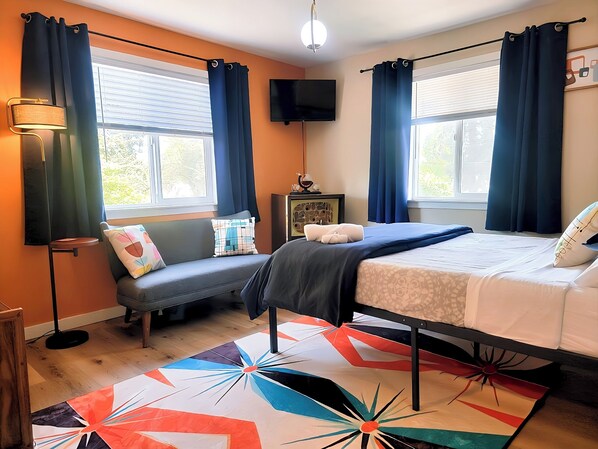A bedroom with a bed, a sofa, a TV, and a patterned rug.