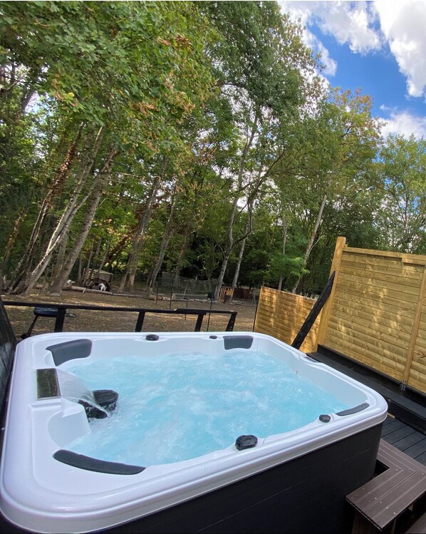 Relax in a hot tub on a raised deck surrounded by lush greenery and a clear view of the surrounding trees.