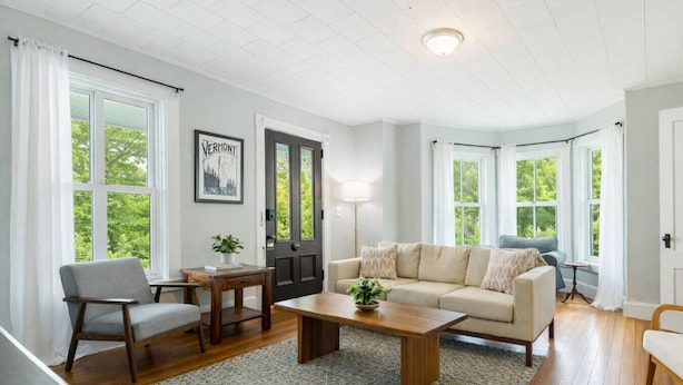 A living room with a sofa, coffee table, and chairs, a door with a dark frame, and a window with a view of trees. - Raspberry Inn · Classic Riverfront Home-Mins to Woodstock & Skiing (Bridgewater)